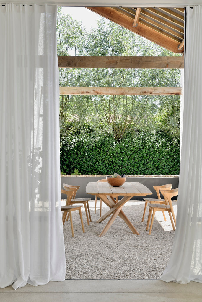 Mikado Outdoor Dining Table with Bok Outdoor Dining Chairs under a natural wood pergola on gravel, styled with a ceramic bowl. - Saffron and Poe, Ethnicraft