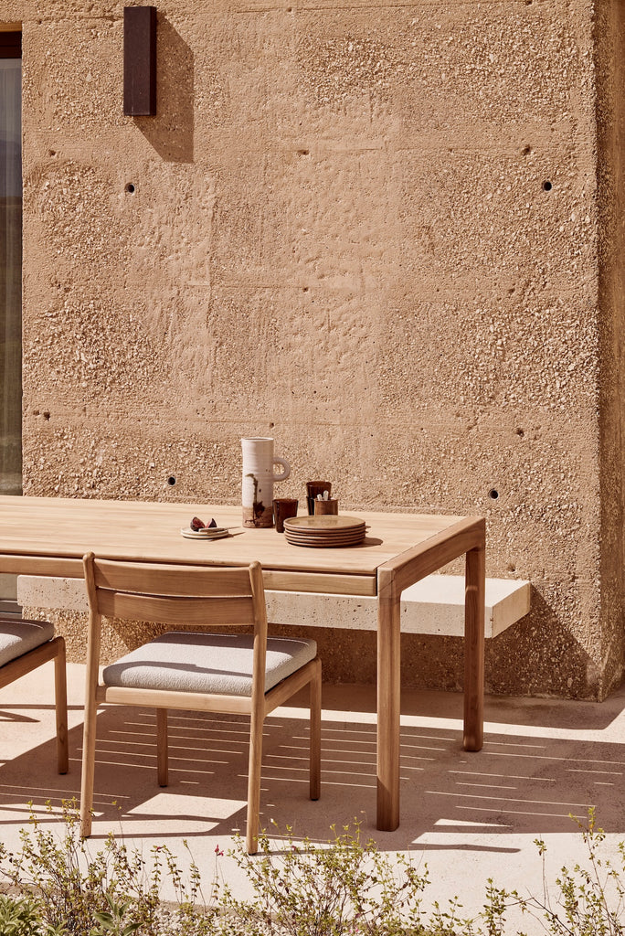 Jack Muir Outdoor Dining Chairs and natural cushion seat with Jack Outdoor Dining Table on an outdoor patio with a natural rock wall. - Saffron and Poe, Ethnicraft