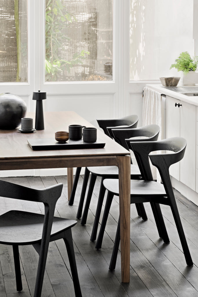 Close up detail view of Darkened Teak Bok Dining Table and Black Oak Bok chairs in dining room with wall of windows behind and decorative objects on table with black wood flooring, with floating table top and beautiful wood joinery. - Saffron and Poe, Ethnicraft