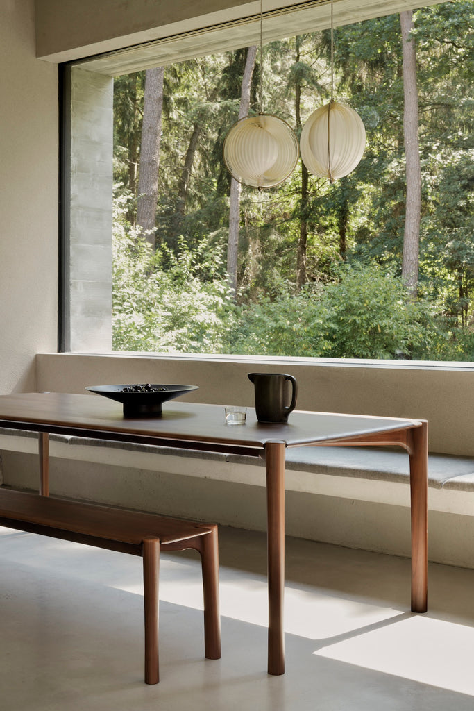 Dark Teak PI Dining Table and bench in modern concrete and plaster dining room with large windows and tall ceilings. - Saffron and Poe, Ethnicraft