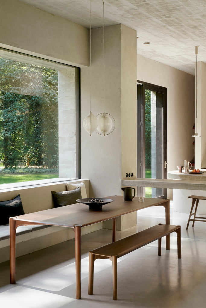 Dark Teak PI Dining Table and bench in modern concrete and plaster dining room with large windows and tall ceilings. - Saffron and Poe, Ethnicraft