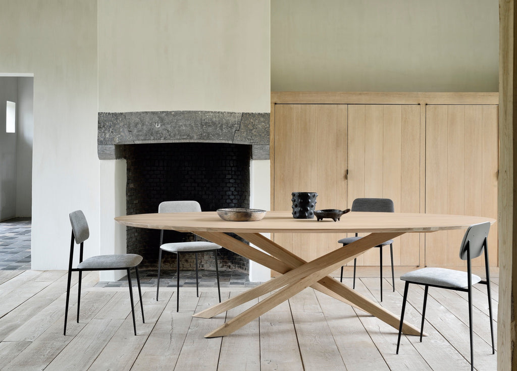 White Oak Oval Mikado Dining Table and in european plastered dining room with exposed rafters and stone fireplace, with objects styled on top. - Saffron and Poe, Ethnicraft