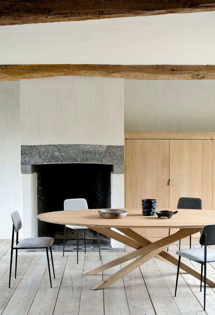 White Oak Oval Mikado Dining Table and in european plastered dining room with exposed rafters and stone fireplace, with objects styled on top. - Saffron and Poe, Ethnicraft