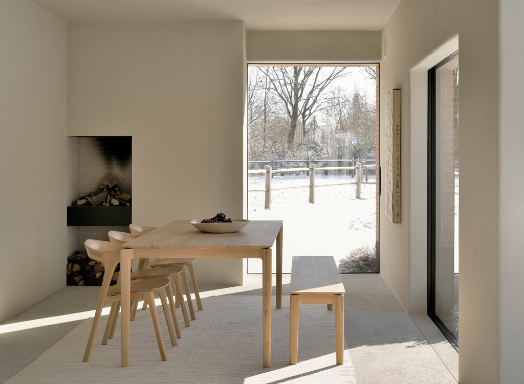White Oak Bok Dining Table in dining room with fireplace and snowy landscape through window, showing floating wood table top. - Saffron and Poe, Ethnicraft