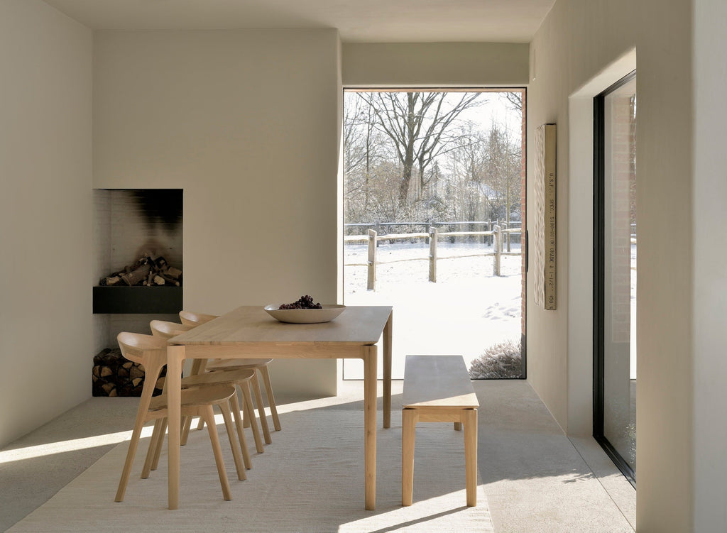 White Oak Bok Dining Table in dining room with fireplace and snowy landscape through window, showing floating wood table top. - Saffron and Poe, Ethnicraft