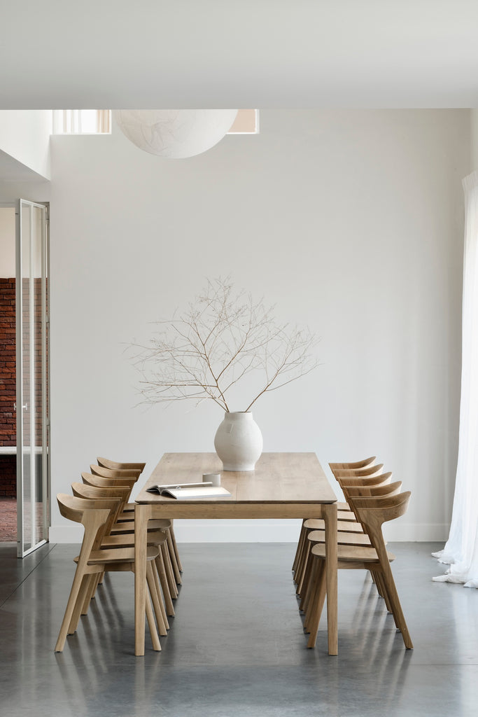 White Oak Bok Dining Table in dining room with high ceilings with vase and open book on table, showing floating wood table top. - Saffron and Poe, Ethnicraft