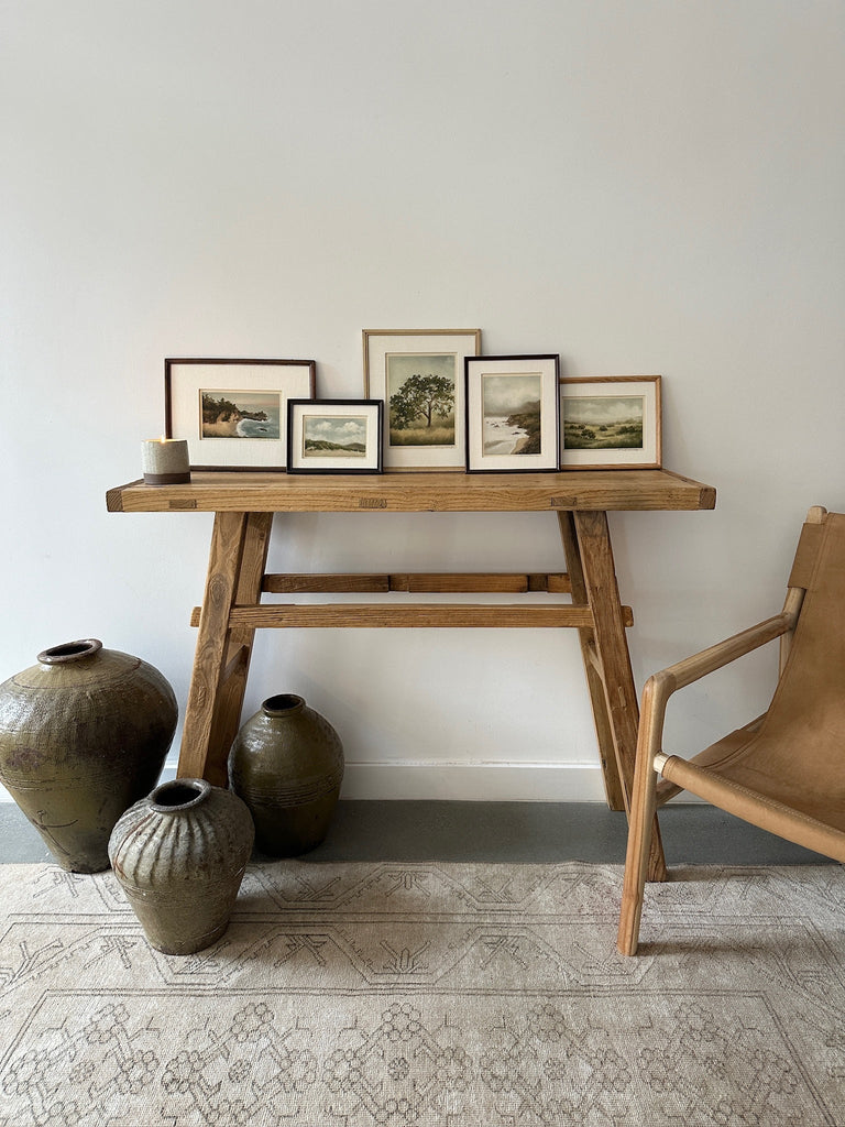 Pastel/Painting in antique frame with linen mat of rolling California golden hills styled on a vintage console with other paintings, with a sling lounge chair next to it. - Saffron and Poe, Lina Gordievsky
