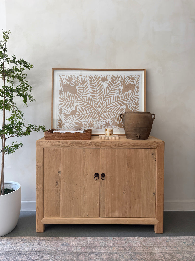 Wooden cabinet with decorative items and antique clay pot against a plain wall. Saffron + Poe