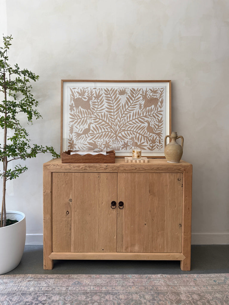 Wooden cabinet with antique Italian vessel and framed textile against a lime washed wall - Saffron + Poe
