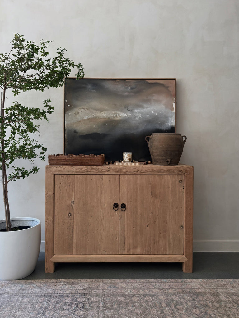 Wooden cabinet with decorative items and an abstract painting against a limewash wall
