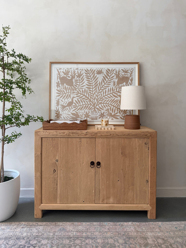 Ostuni Ceramic Table Lamp in Terracotta with oatmeal linen shade on an antique cabinet styled with decorative items against a limewashed wall. - Saffron + Poe