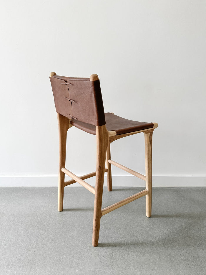 Back side view of the Wrapped Leather Counter Stool on concrete flooding with white wall backdrop. - Saffron and Poe