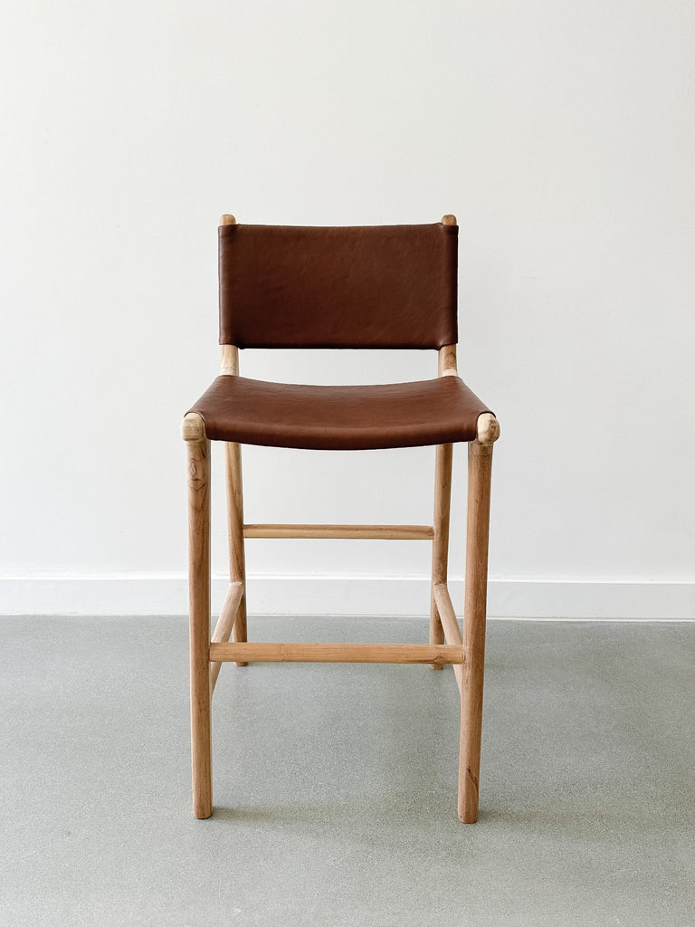Front view of the Wrapped Leather Counter Stool on concrete flooding with white wall backdrop. - Saffron and Poe