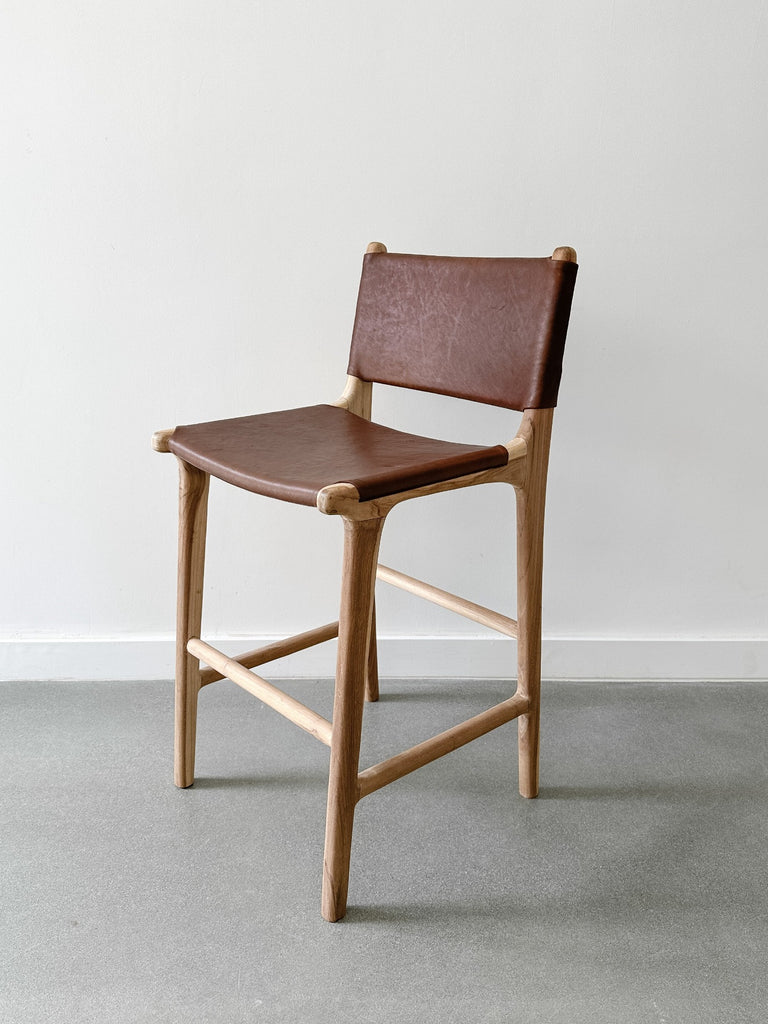 Side view of the Wrapped Leather Counter Stool on concrete flooding with white wall backdrop. - Saffron and Poe