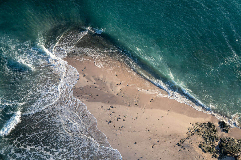 Aerial photo of the aqua blue ocean against a sandy shore by Mika Street for Saffron and Poe