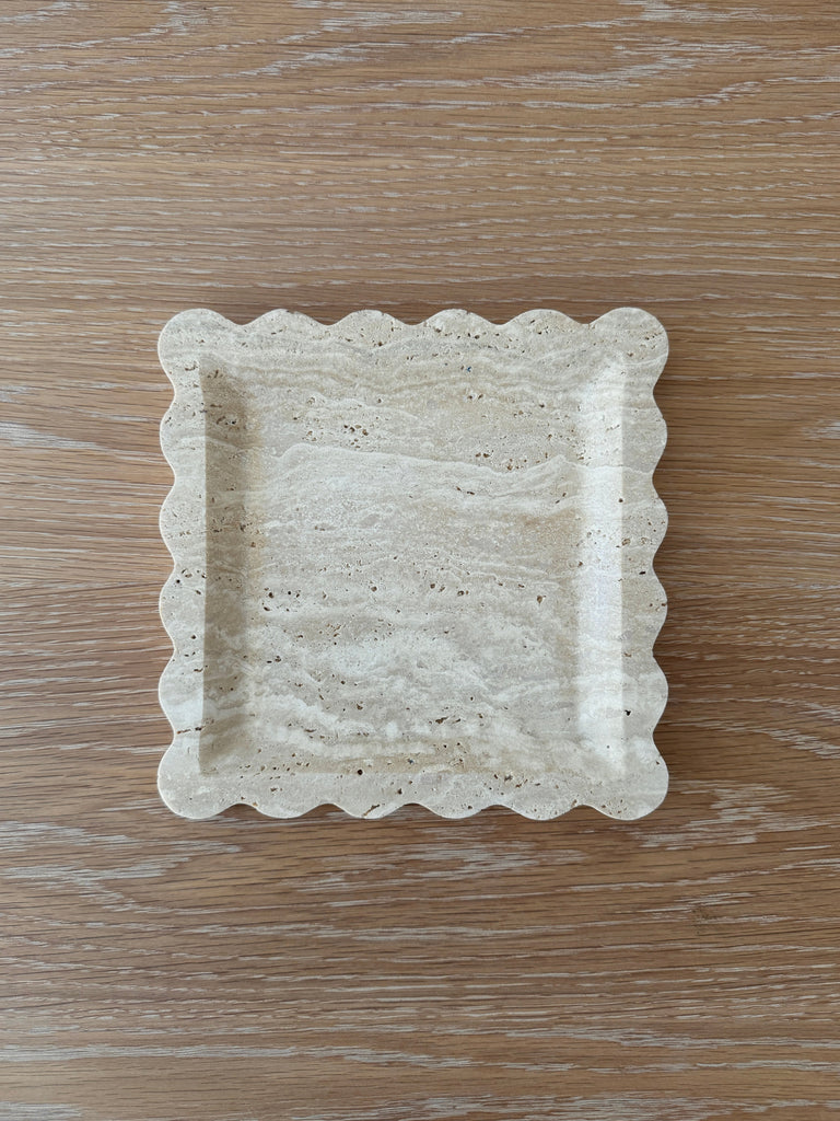 Travertine tray with scalloped edge on a wooden surface