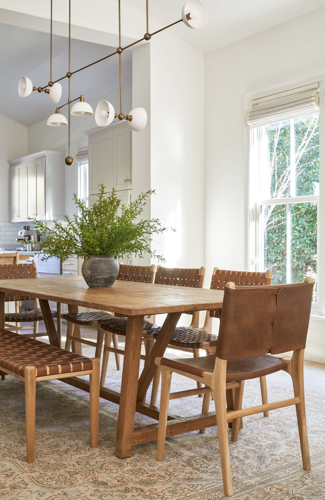 Our Stretched Leather and Teak Wood Sofía Dining Chair styled in a dining room with dining table, light fixture and rug - Saffron + Poe