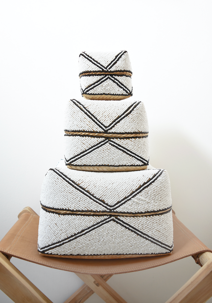 Three Hand-Beaded Bali Storage Baskets in Solid White stacked on each other sitting on a leather strapped stool. Handmade in Bali using woven bamboo- Saffron and Poe