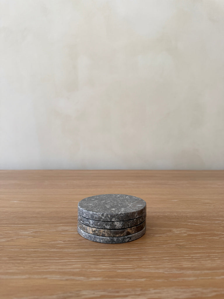 Stack of dary grey round stone coasters on a wooden surface with a plain background