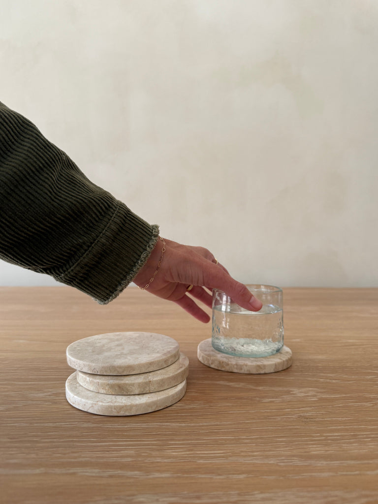 Person placing a glass on a stack of stone coasters on a wooden surface.