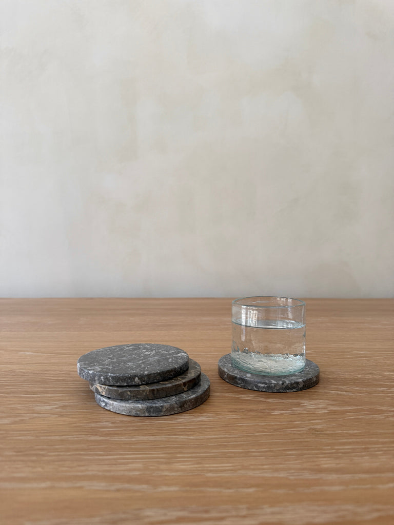 Set of stone coasters on a wooden surface with a glass of water.