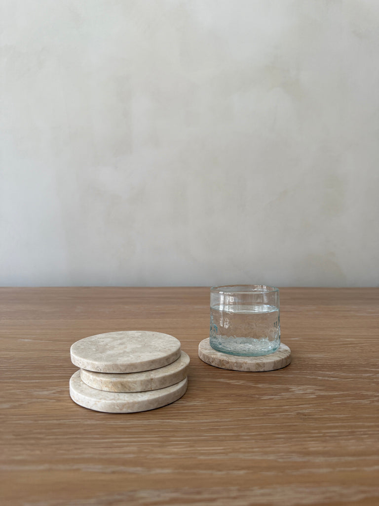 Set of marble coasters on a wooden surface with a glass of water.