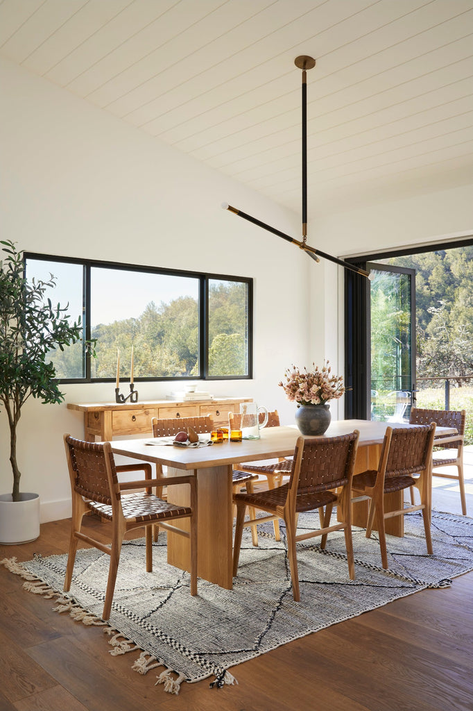 Styled photo of Woven Leather Dining Chair in a dining room setting with Live Edge Oak Dining Table, Vintage Storage Console, Antique Clay Pot, and Moroccan Flat Weave Kilim Rug. - Saffron and Poe
