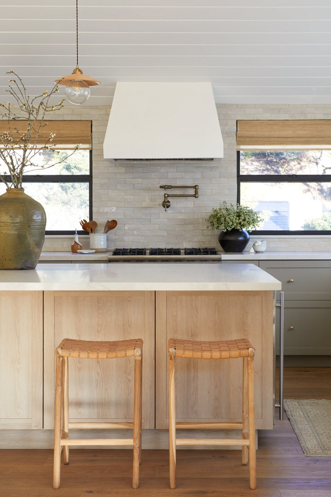 Backless Woven Leather Counter Stool in Beige styled in a kitchen setting with Antique Clay Pot, Vintage Mijiu Jar, Ceramic Utensil Jar, and Ceramic Olive Oil Bottle. -Saffron and Poe