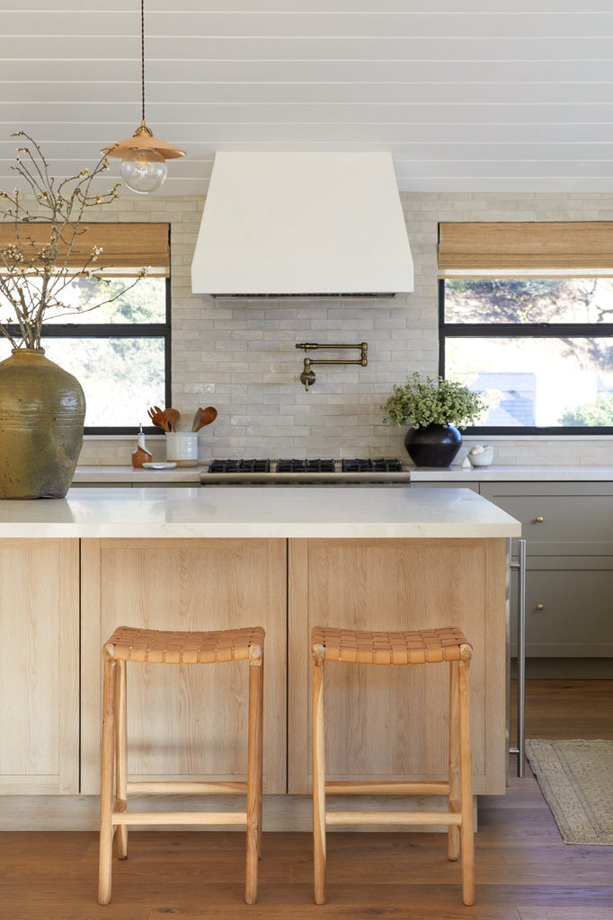 Backless Woven Leather Counter Stool in Beige styled in a kitchen setting with Antique Clay Pot, Vintage Mijiu Jar, Ceramic Utensil Jar, and Ceramic Olive Oil Bottle. -Saffron and Poe