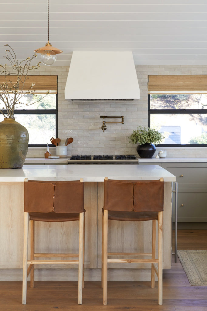 Wrapped Leather Counter Stools styled in a kitchen setting with Antique Clay Pot, Vintage Mijiu Jar, Ceramic Utensil Jar, and Ceramic Olive Oil Bottle. -Saffron and Poe 