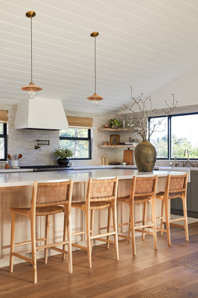 Woven Leather Counter Stools in Beige styled in a kitchen setting around a large island with Antique Clay Pot, Vintage Mijiu Jar, Ceramic Utensil Jar, and Ceramic Olive Oil Bottle. -Saffron and Poe
