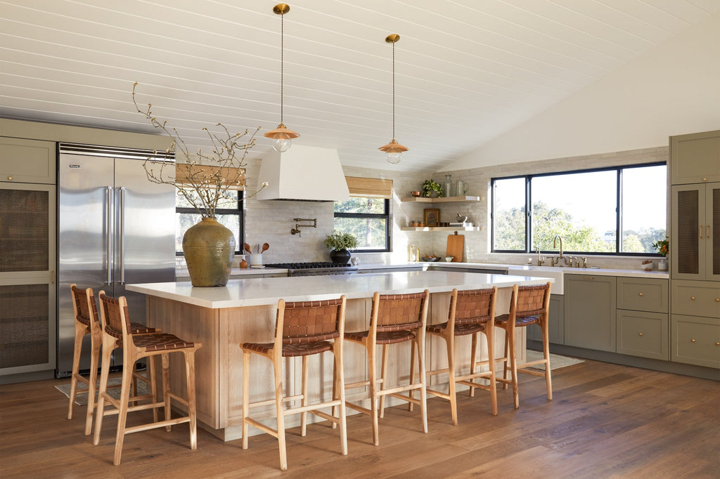 Woven Leather Counter Stools in Saddle styled in a kitchen setting around a large island with Antique Clay Pot, Vintage Mijiu Jar, Ceramic Utensil Jar, and Ceramic Olive Oil Bottle. -Saffron and Poe