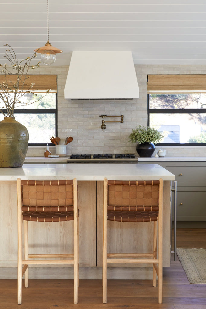 Woven Leather Counter Stools in Saddle styled in a kitchen setting with Antique Clay Pot, Vintage Mijiu Jar, Ceramic Utensil Jar, and Ceramic Olive Oil Bottle. - Saffron and Poe
