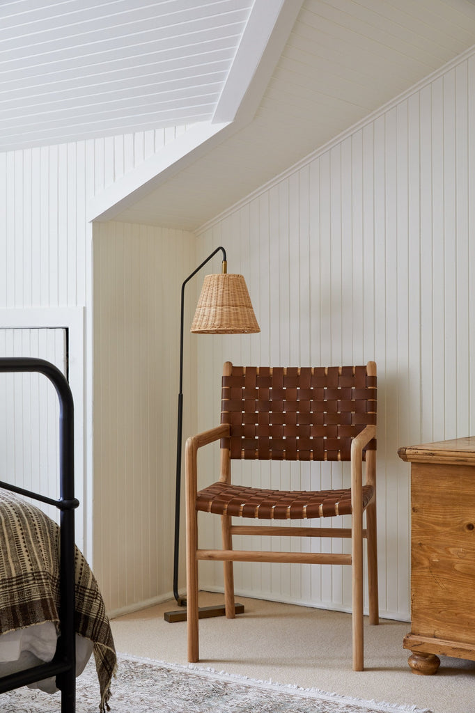 Woven Leather Dining Arm Chair in Saddle styled in a bedroom setting with a woven floor lamp. - Saffron and Poe