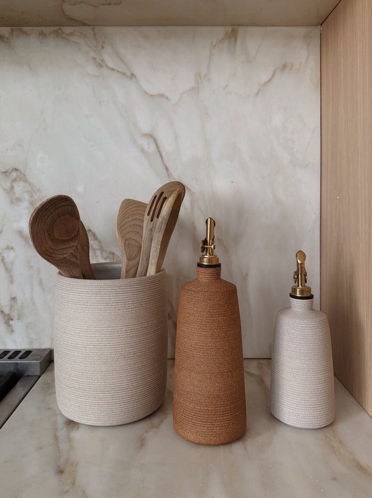 Olive oil bottle with balsamic vinegar bottle and utensil jar with wooden spoons on a marble countertop