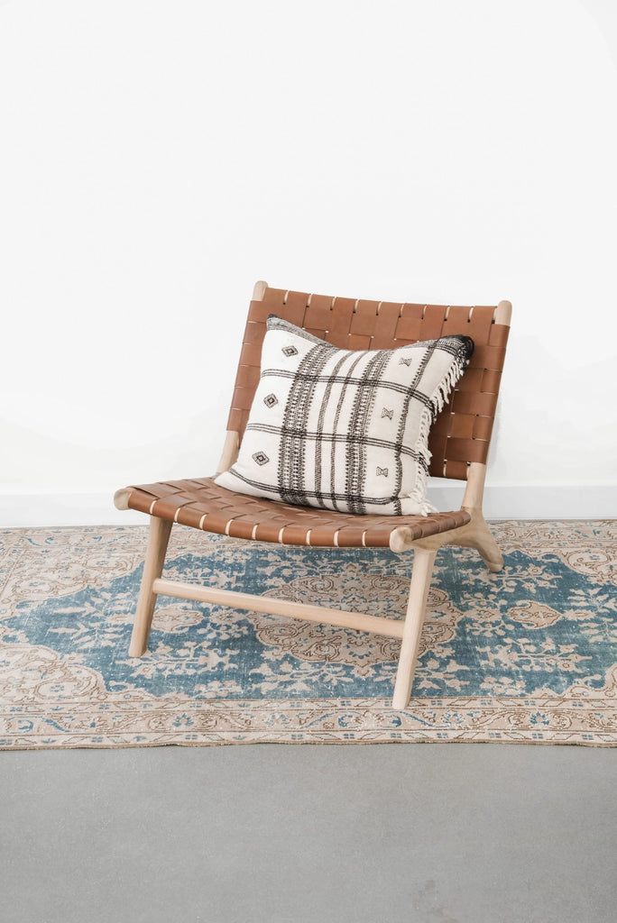 Side angle view of our Woven Leather Strap Lounge Chair in Saddle styled with a pillow and rug. Handmade in Bali with Teak wood and vegetable-tanned leather imported from Java. - Saffron and Poe