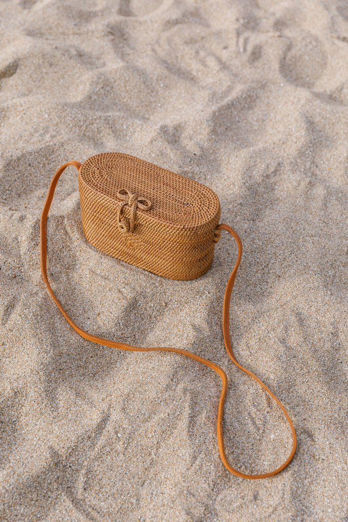 Angled top view of Tenganan Basket Cross Body - Oval - against a beach background. - Saffron and Poe
