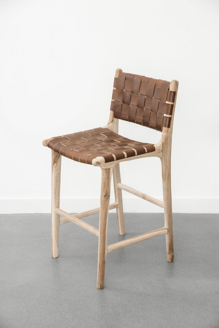Side angle view of our Woven Leather Strap Counter Stool - Saddle on a white background. Handcrafted in Bali using teak wood and leather. - Saffron and Poe