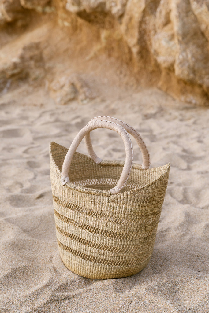 Angled view of Woven Sisal Farmer's Market Tote with a beach background. - Saffron and Poe