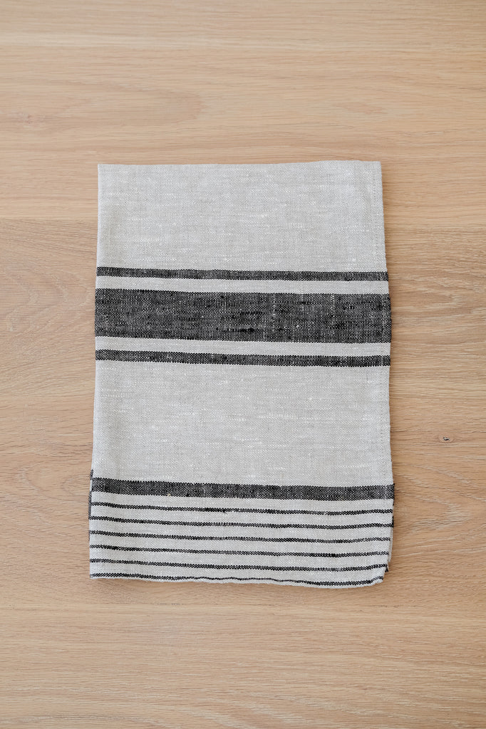 Front folded Dark Grey Stripe Linen Hand Towel (Set of 2) on a White Oak Dining Table. - Saffron and Poe