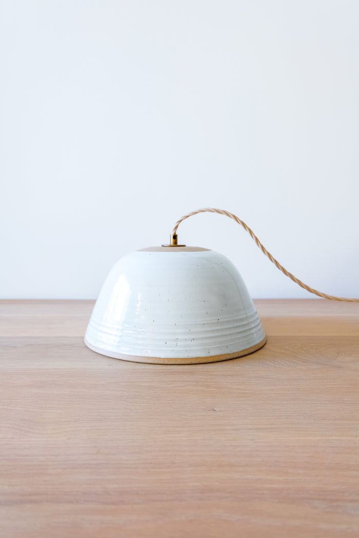 Front view of Hand Thrown Ceramic Pendant Light on an Oak Dining Table against a white wall. - Saffron and Poe