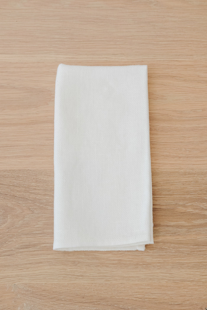 Front Ivory Linen Napkin on a White Oak Dining Table. - Saffron and Poe