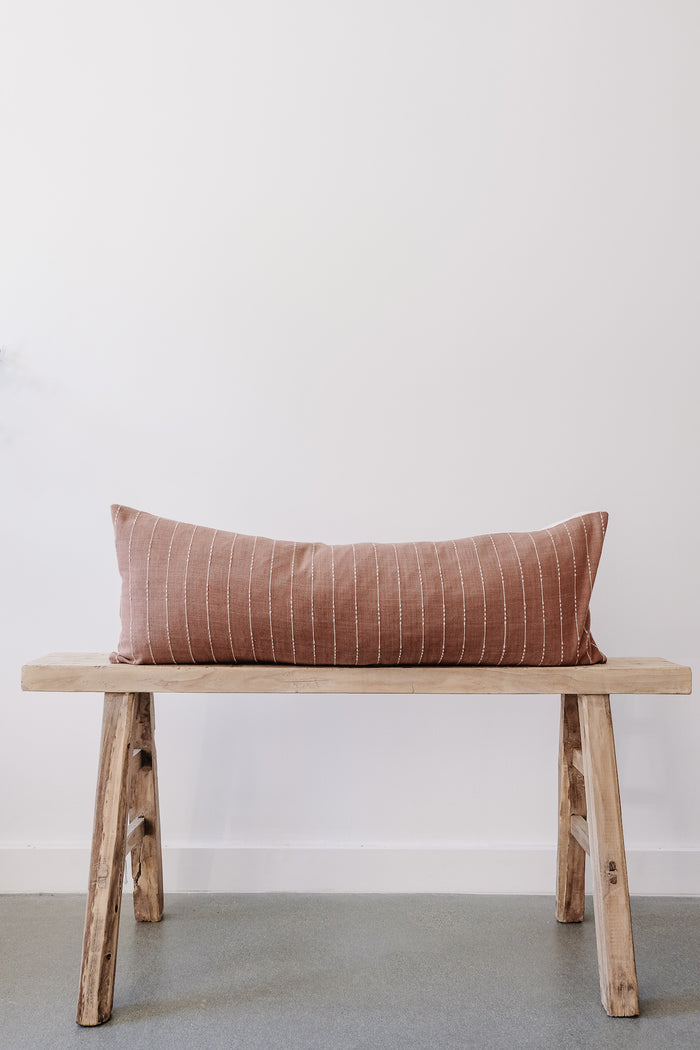 Front view of No. 13 - Hmong Hemp Lumbar Pillow - Extra Long on an Antique Bench against a white wall. - Saffron and Poe