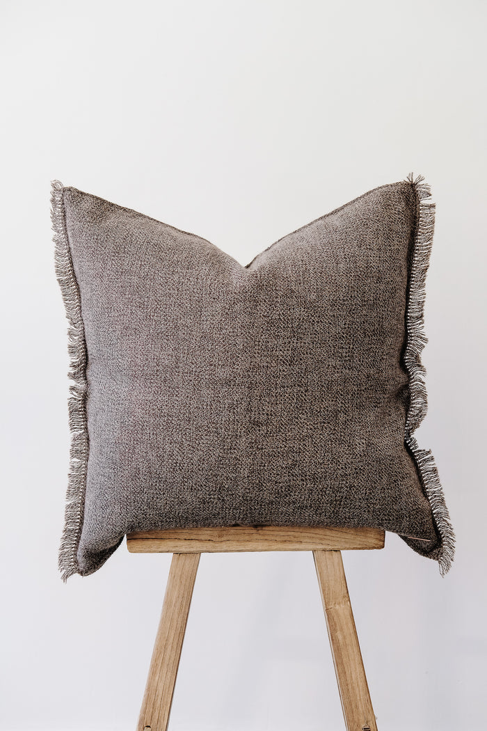 Front view of No. 29 - Baby Alpaca Pillow - Dark Brown on an Antique Stool against a white wall. - Saffron and Poe