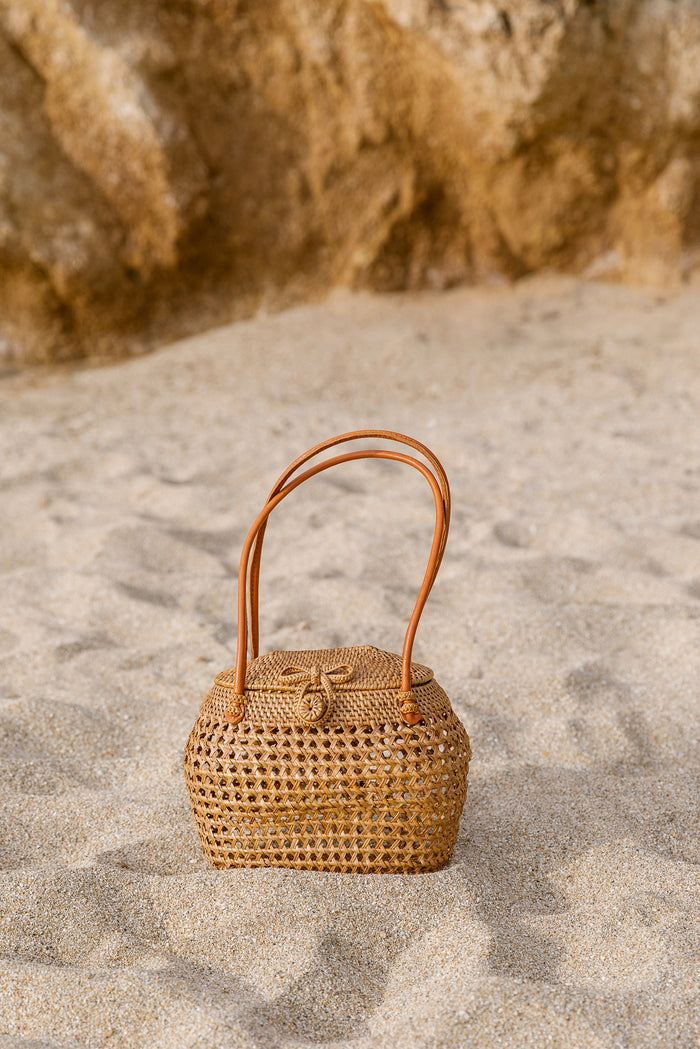 Front view of Tenganan Basket Clasp Handbag on a beach. - Saffron and Poe