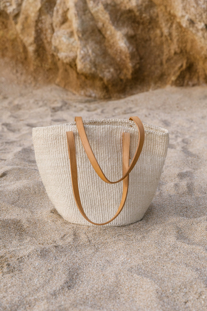 Front view of Woven Sisal and Leather Tote with a beach background. - Saffron and Poe