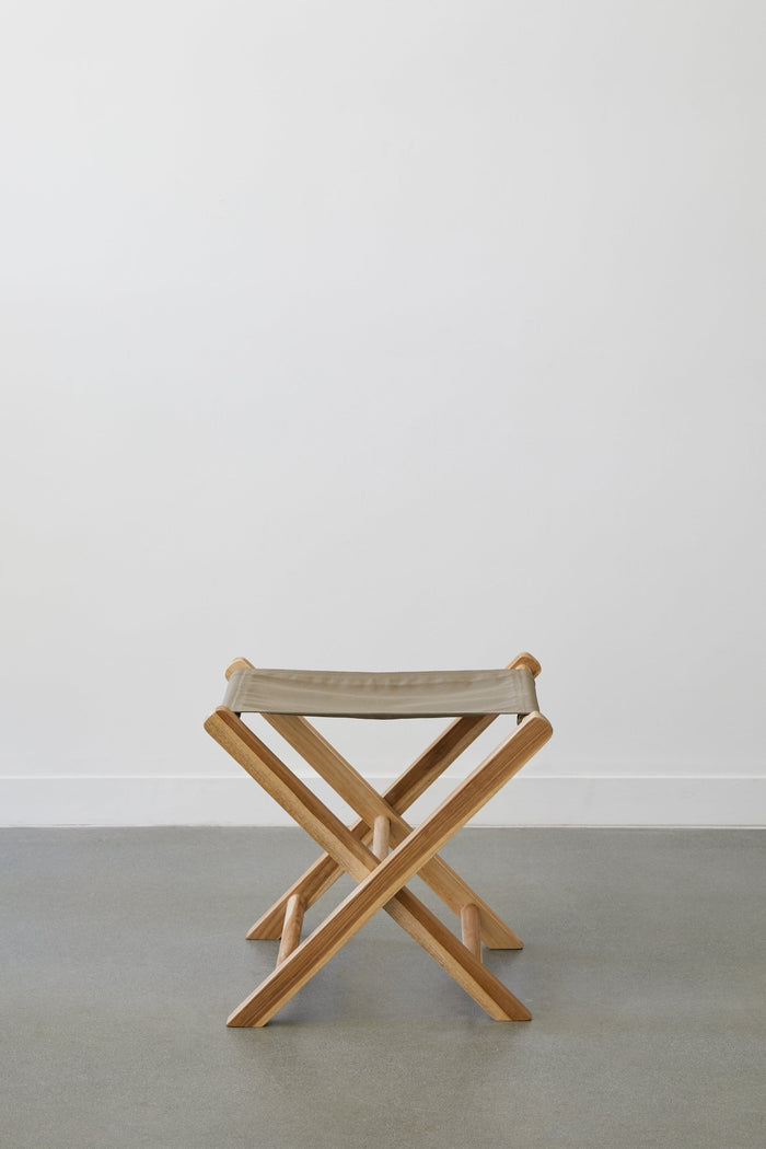 Front view of Taupe Canvas Folding Stool against white background on concrete flooring. - Saffron and Poe