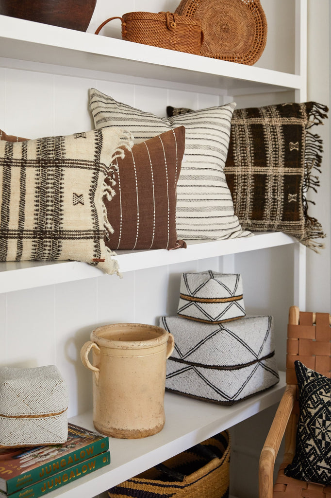 Italian confit pot on white shelves next to bali beaded baskets and under embroidered pillows.