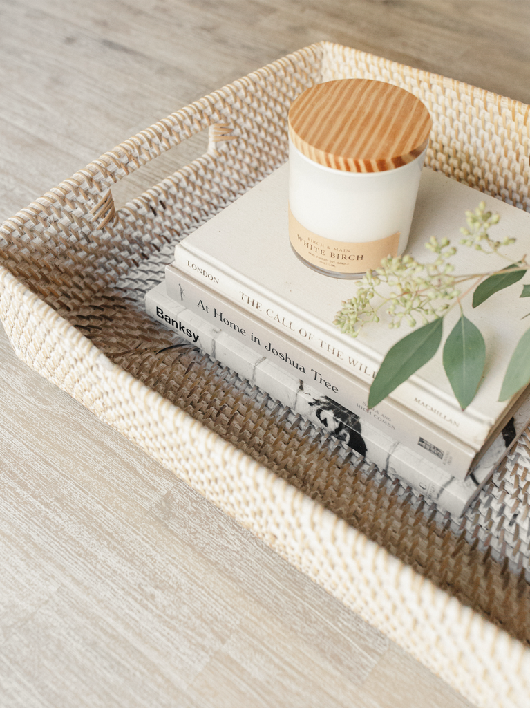 Detailed view of whitewashed Lombok Basket Tray with plant, candle and books. Handwoven in Bali with rattan. - Saffron and Poe