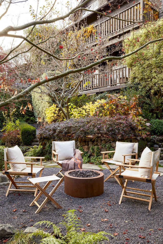 Outdoor angled view of four Oatmeal Canvas Director's Chairs and one Oatmeal Folding Stool fireside on gravel. Note: All outdoor photos display Ivory colorway.  -Saffron and Poe
